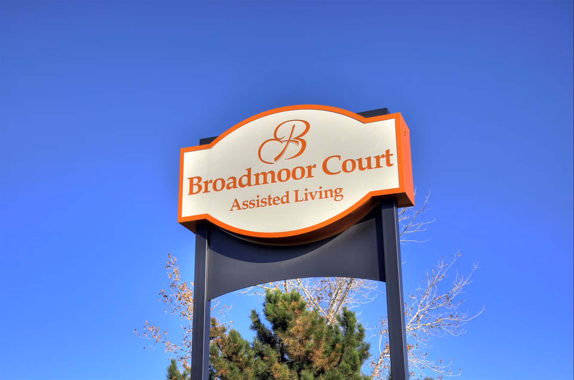 Outdoor sign reading "Broadmoor Court Assisted Living" set against a clear blue sky.