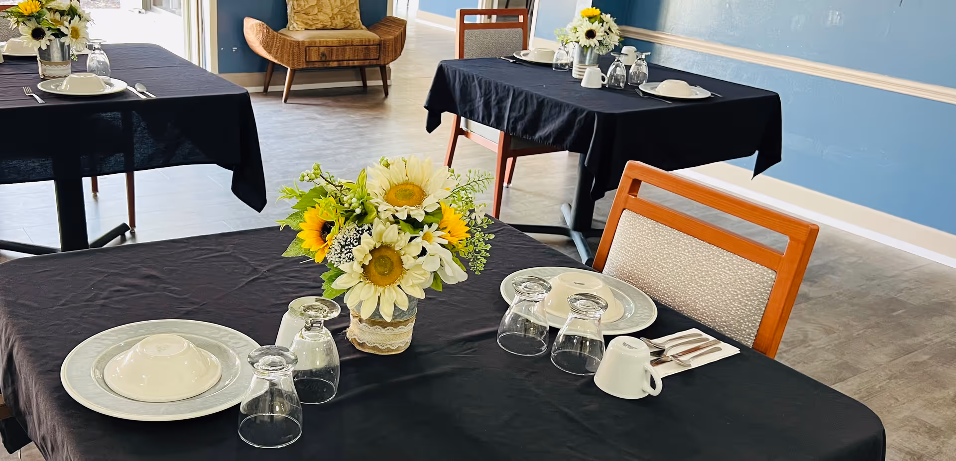 Dining room tables set with plates, glasses and sunflower centerpieces in a communal dining area.