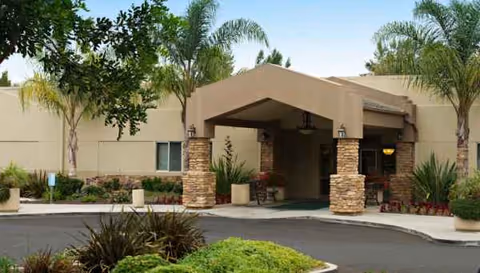 Front entrance of Carmel Mountain Rehabilitation and Healthcare Center with a covered walkway and landscaping.