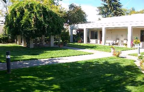 A sunny outdoor courtyard with a lawn, path, and a white building patio.