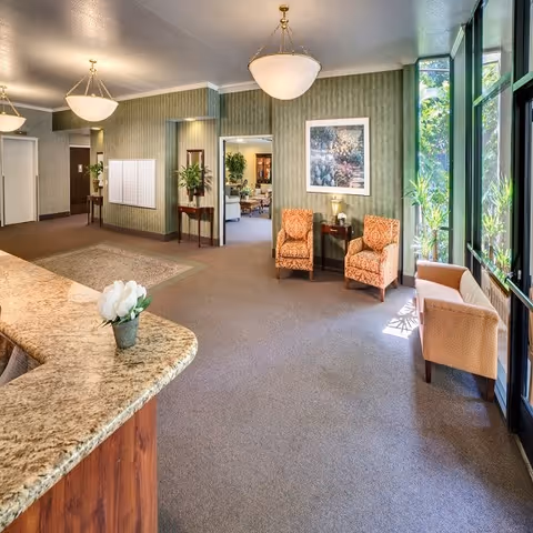 Bright reception lobby with a granite front desk, upholstered chairs, and floor-to-ceiling windows.