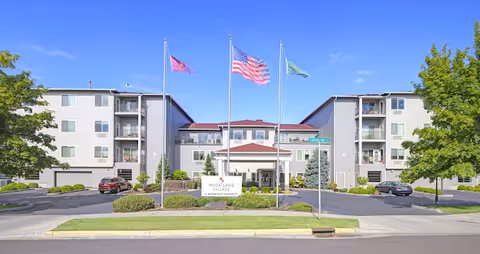 Exterior view of Wheatland Village senior living facility with a three-flag display.