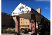Entrance canopy with a sign reading 'Mount Alverno Center' supported by brick columns in front of a multi-story brick building under a blue sky.
