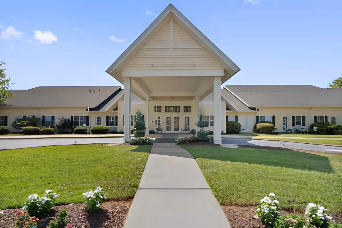 Front entrance of an assisted living building with a covered portico, walkway, and landscaped lawn.