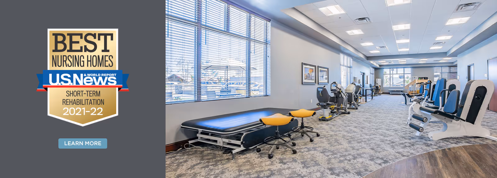 A spacious rehabilitation gym with exercise equipment including stationary bikes, leg press machines, and therapy tables. Large windows allow natural light to fill the room, and framed artwork is displayed on the walls.