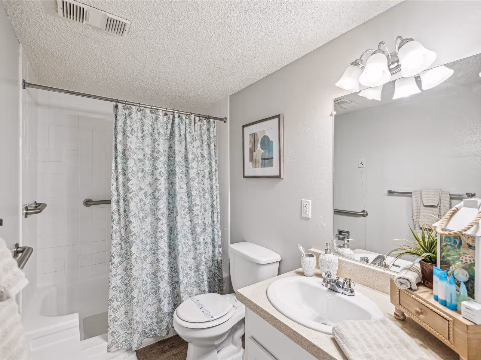 A well-lit bathroom featuring a shower with a patterned curtain, a white toilet, and a sink with toiletries and decorative items on the countertop.