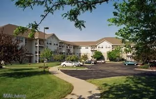 Exterior view of a multi-story senior living facility named Sherman Glen with a parking lot in front, surrounded by green lawns and trees under a clear blue sky.