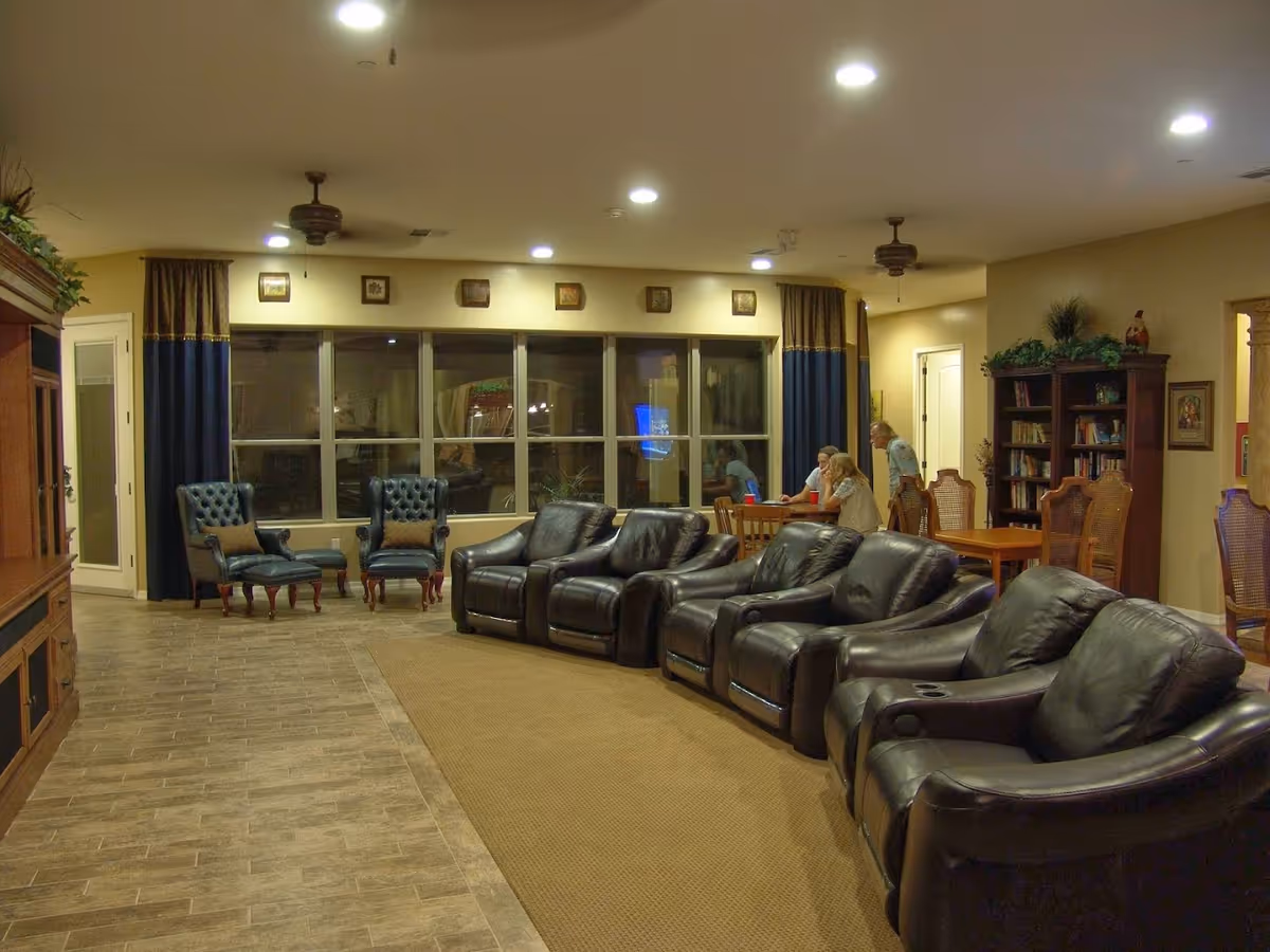 Cozy senior living lobby with leather lounge seating, tables, a bookshelf, and residents gathering.