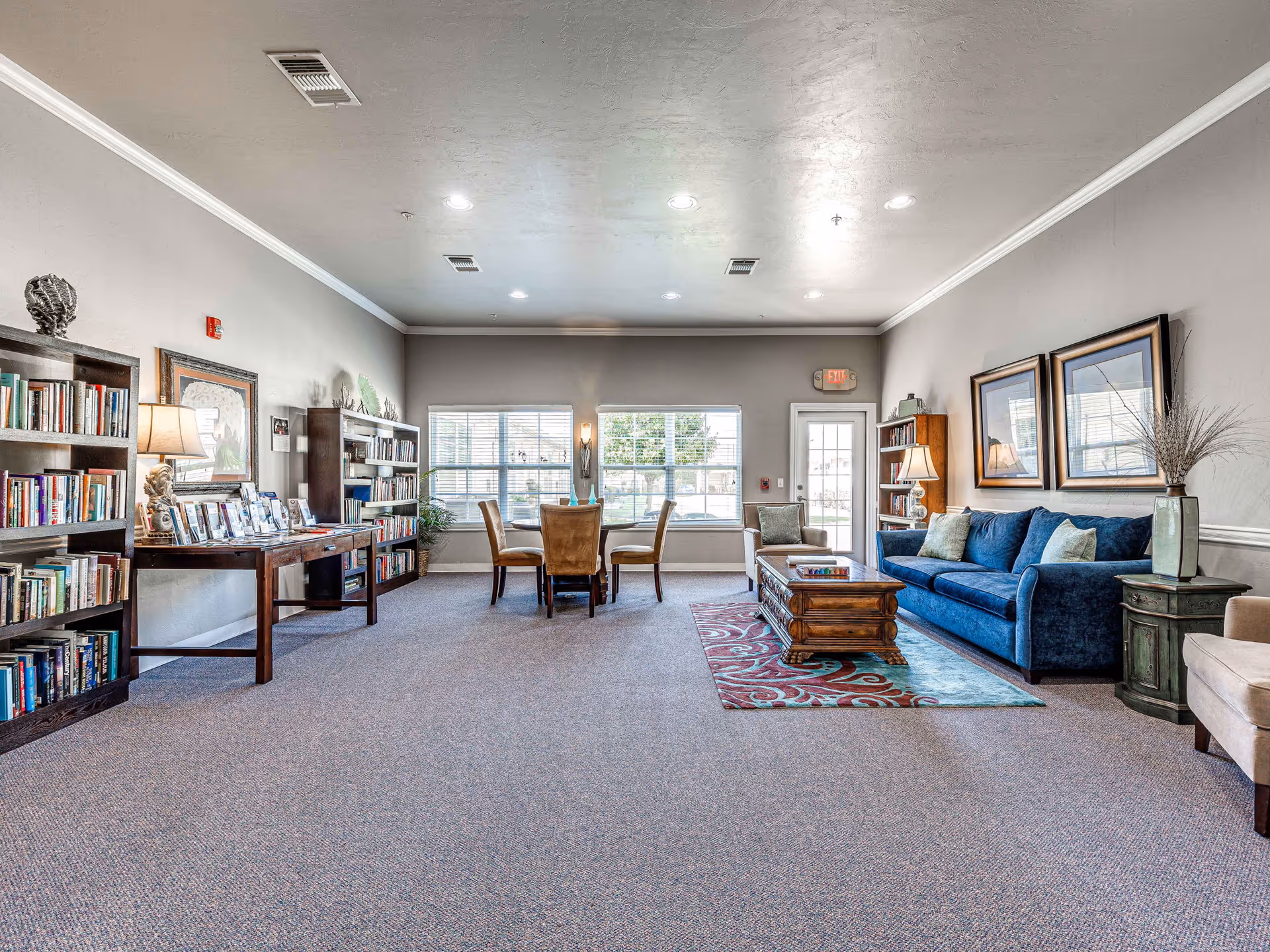 Spacious senior living lounge with blue sofa, coffee table, bookshelves and windows.