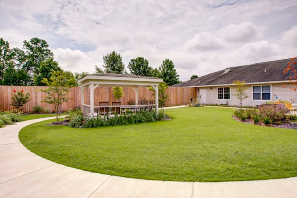 Well-maintained courtyard with a covered gazebo, curved sidewalk, green lawn, landscaping, and a single-story building in the background.