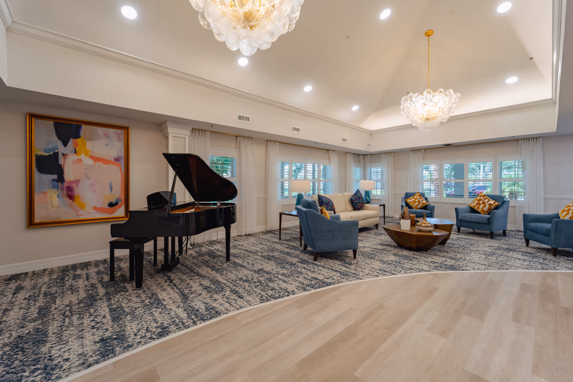 Spacious furnished lounge with a grand piano, sofas and armchairs around a coffee table, chandeliers, and large windows.