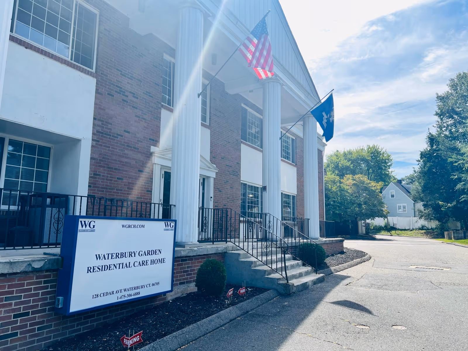 Exterior view of Waterbury Gardens residential care home showing entrance and flags.
