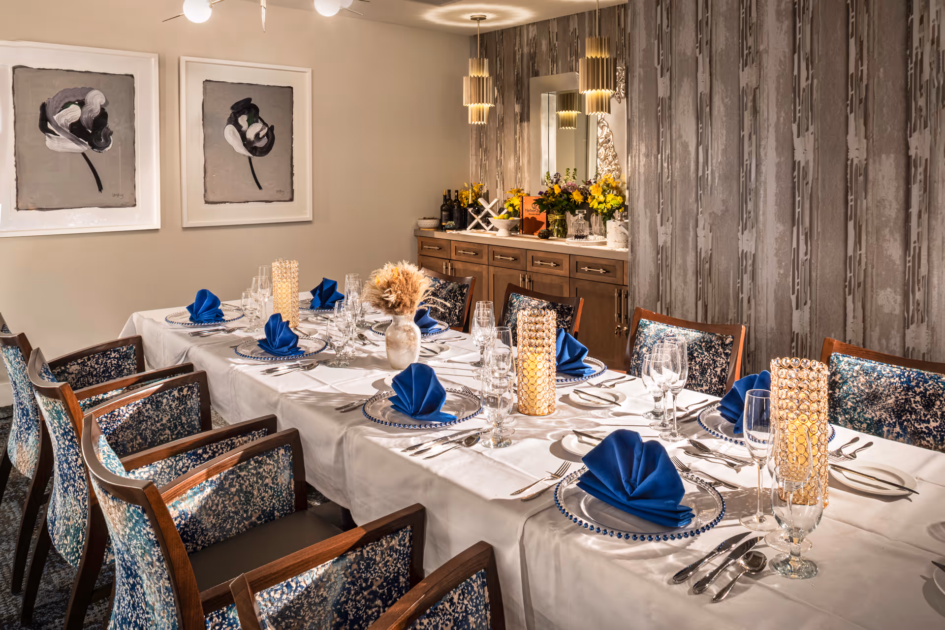 Elegantly set dining table with blue napkins, glassware, and patterned chairs in a decorated dining room.