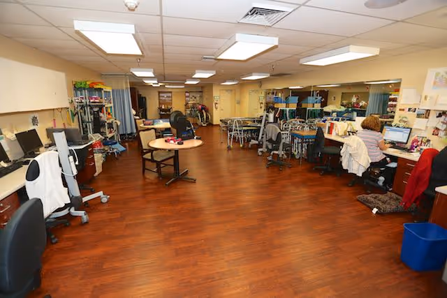 Large interior care room with wood flooring, desks and computers, medical equipment and seating arranged along the sides.