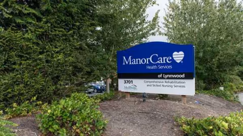 Blue ManorCare Health Services sign on landscaped grounds outside Lynnwood facility.