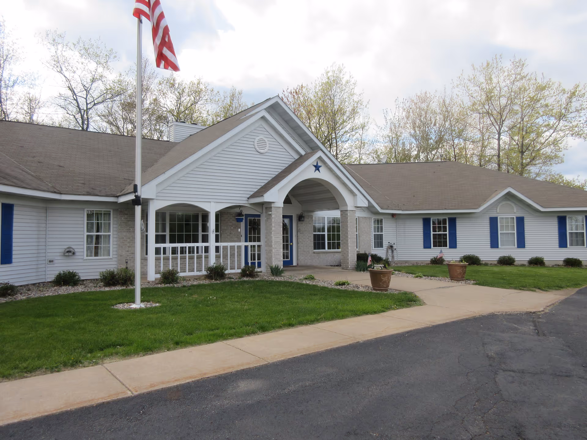 Single-story white building with a covered porch entrance, American flag, and landscaped lawn.