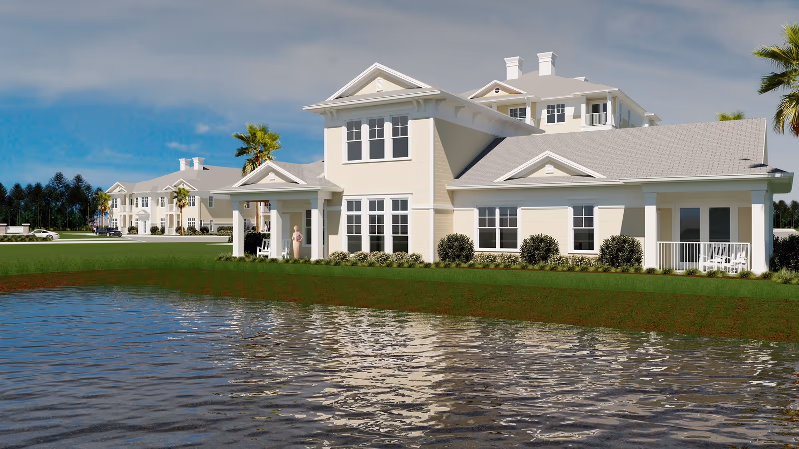 A light-colored multi-story senior living building with porches and windows sits beside a reflective pond under a blue sky.