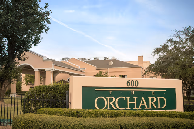 Exterior view of The Orchard facility showing a large sign with the name and address number 600 in front of a beige building with trees and bushes around.