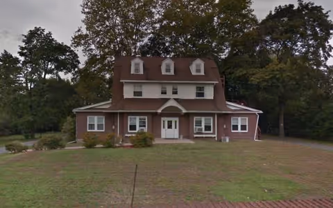 Red-brick building with dormer windows sits on a grassy lawn.