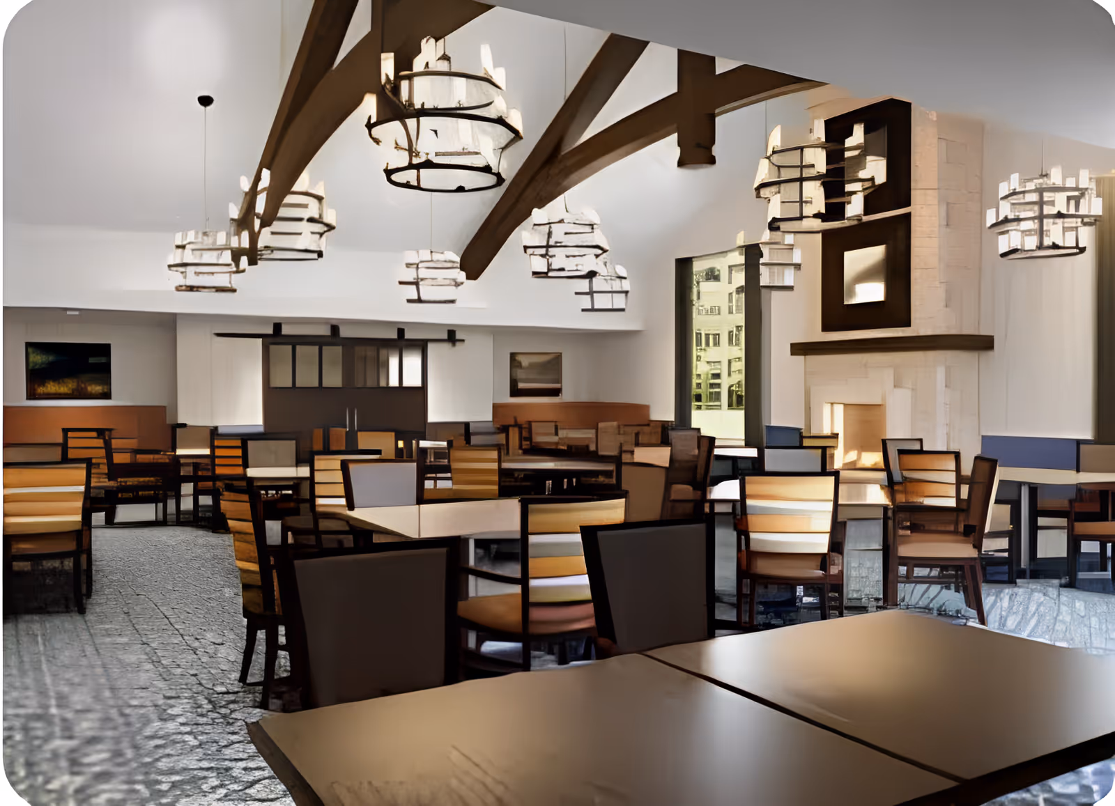 Spacious dining room with multiple tables and chairs, vaulted ceiling with wooden beams and chandeliers, and a fireplace.