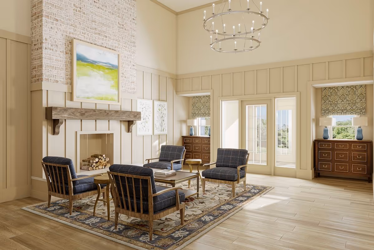 A bright and spacious living room with high ceilings, featuring a stone fireplace with a wooden mantel, four wooden armchairs with dark blue cushions arranged around a wooden coffee table on a patterned area rug. The room has light-colored walls with decorative paneling, two wooden dressers with blue lamps on either side of a set of French doors leading outside, and a modern circular chandelier hanging from the ceiling.