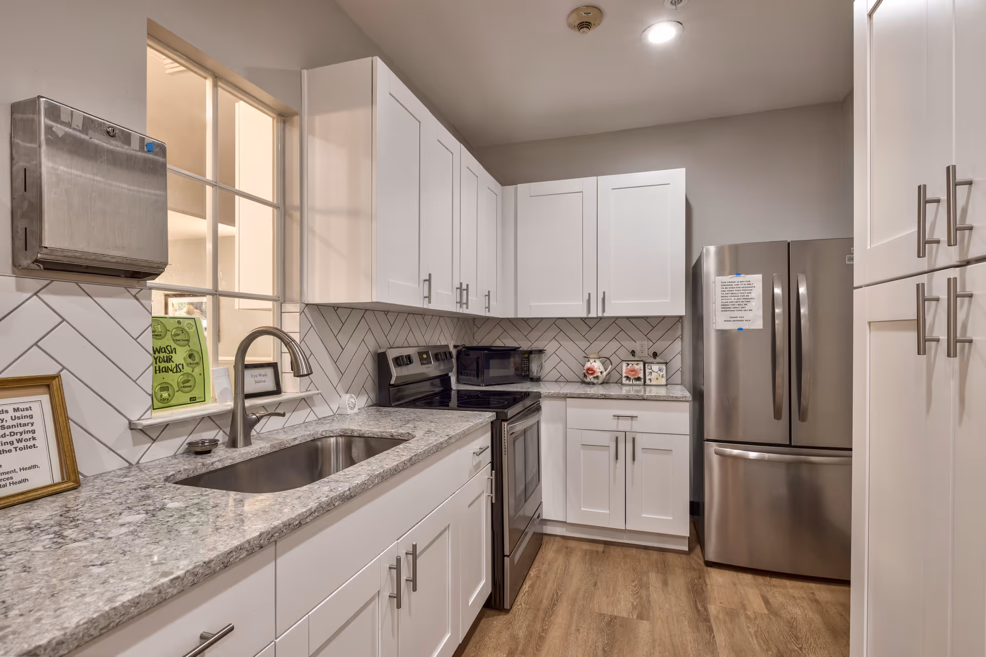 Bright modern kitchen featuring white shaker cabinets, stainless steel refrigerator and stove, a granite countertop with undermount sink, and a herringbone tile backsplash.