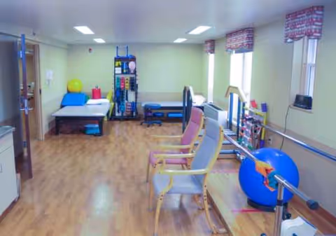 Therapy and rehabilitation room with exercise equipment, chairs, mats, and windows.