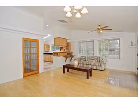 Open-plan living room and kitchen with hardwood floors, a striped sofa, coffee table, ceiling fan, and French doors.