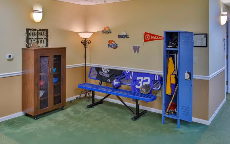 Hallway seating area with a blue bench, open blue locker holding sports gear, and a wooden cabinet against a beige wall with sports-themed decor.
