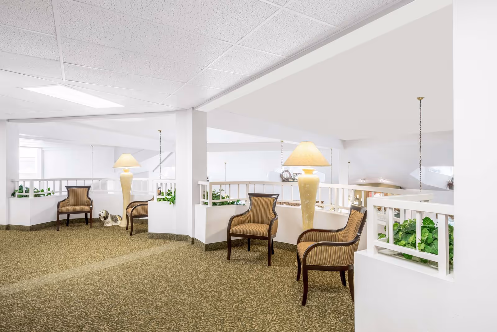 Bright open sitting area with striped armchairs, tall lamps, white railings and potted plants.