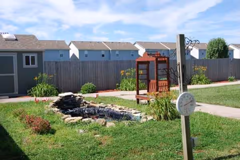 Outdoor courtyard with a stone waterfall feature, a wooden structure, and trimmed lawn.