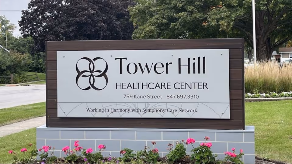 A freestanding outdoor sign for Tower Hill Healthcare Center on a landscaped lawn with flowers.