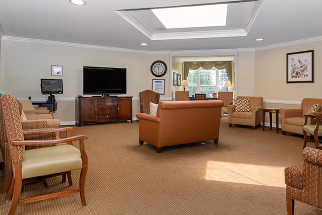 Spacious senior living common room with sofas, armchairs, a television and a skylight.