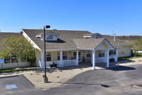 Single-story senior living facility with a covered entrance, parking, and landscaped surroundings.