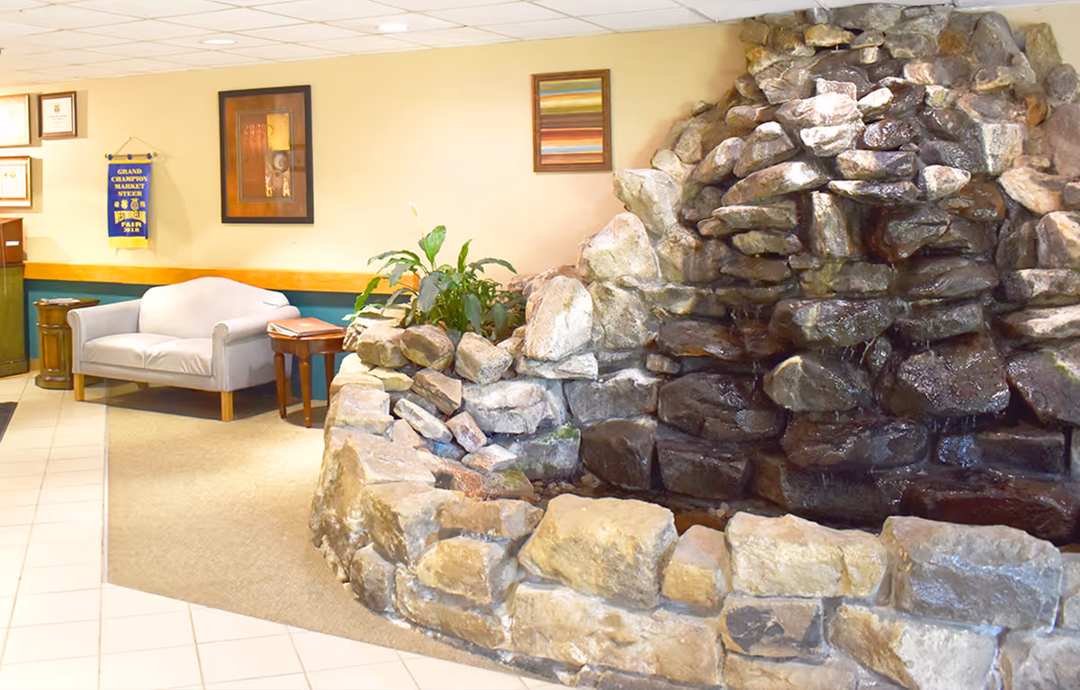Interior lobby area with a large stone indoor water feature, a small sofa, side table, plants and framed wall art.