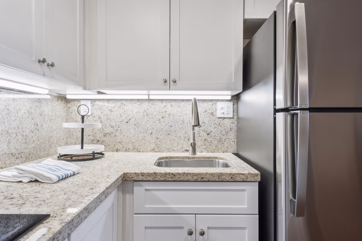 Granite kitchen countertop with sink, white cabinets, and stainless steel refrigerator.