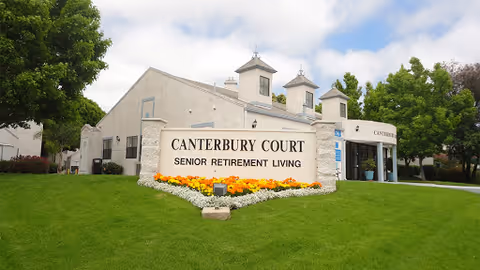 Front entrance and sign for Canterbury Court senior retirement living with manicured lawn and flowers.