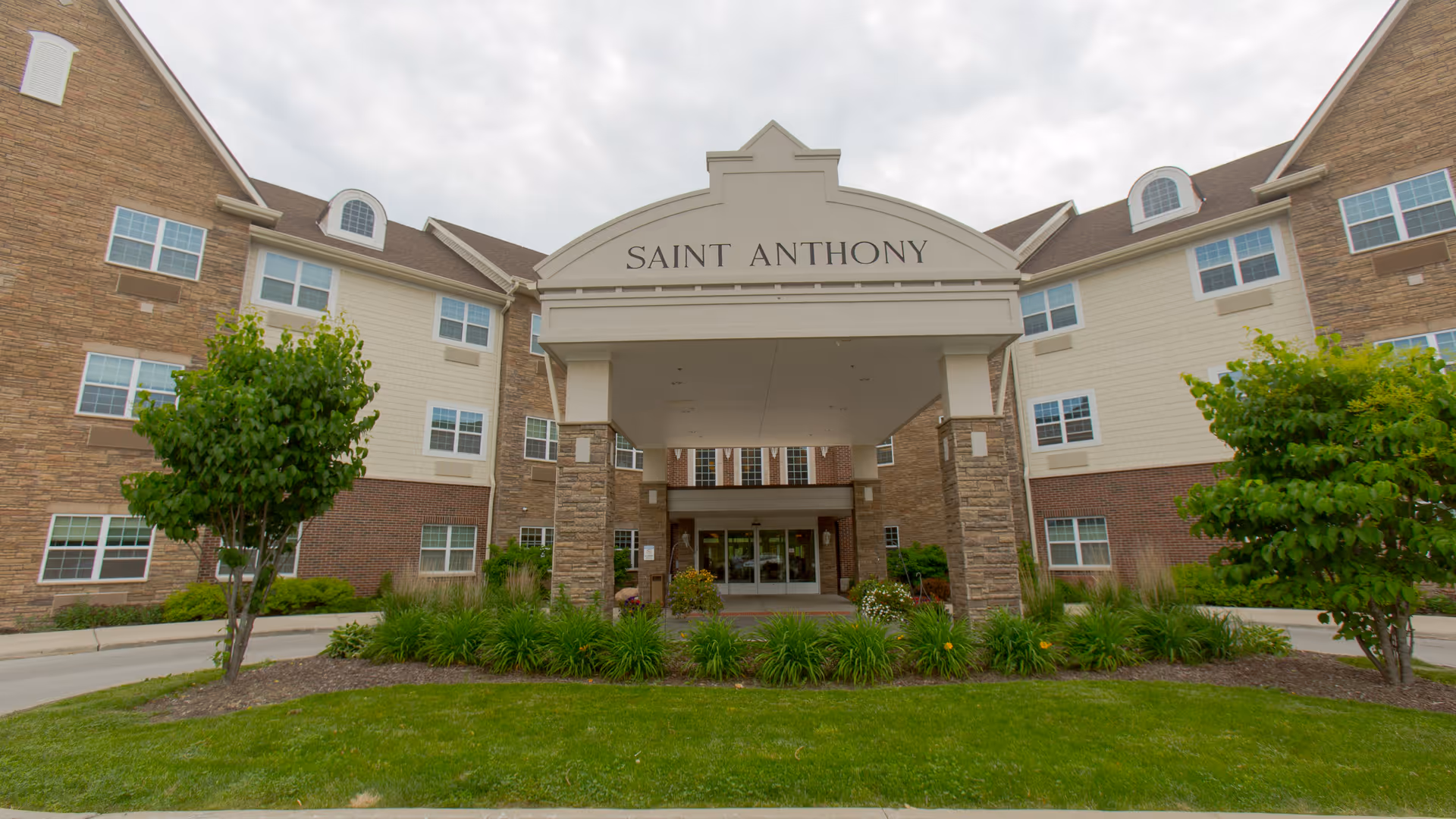 Front entrance of the Saint Anthony senior living building with a covered portico and landscaped lawn.