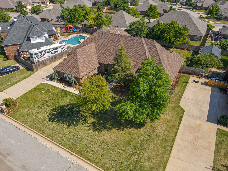Aerial view of a brown-roofed house with surrounding trees and curved driveway.