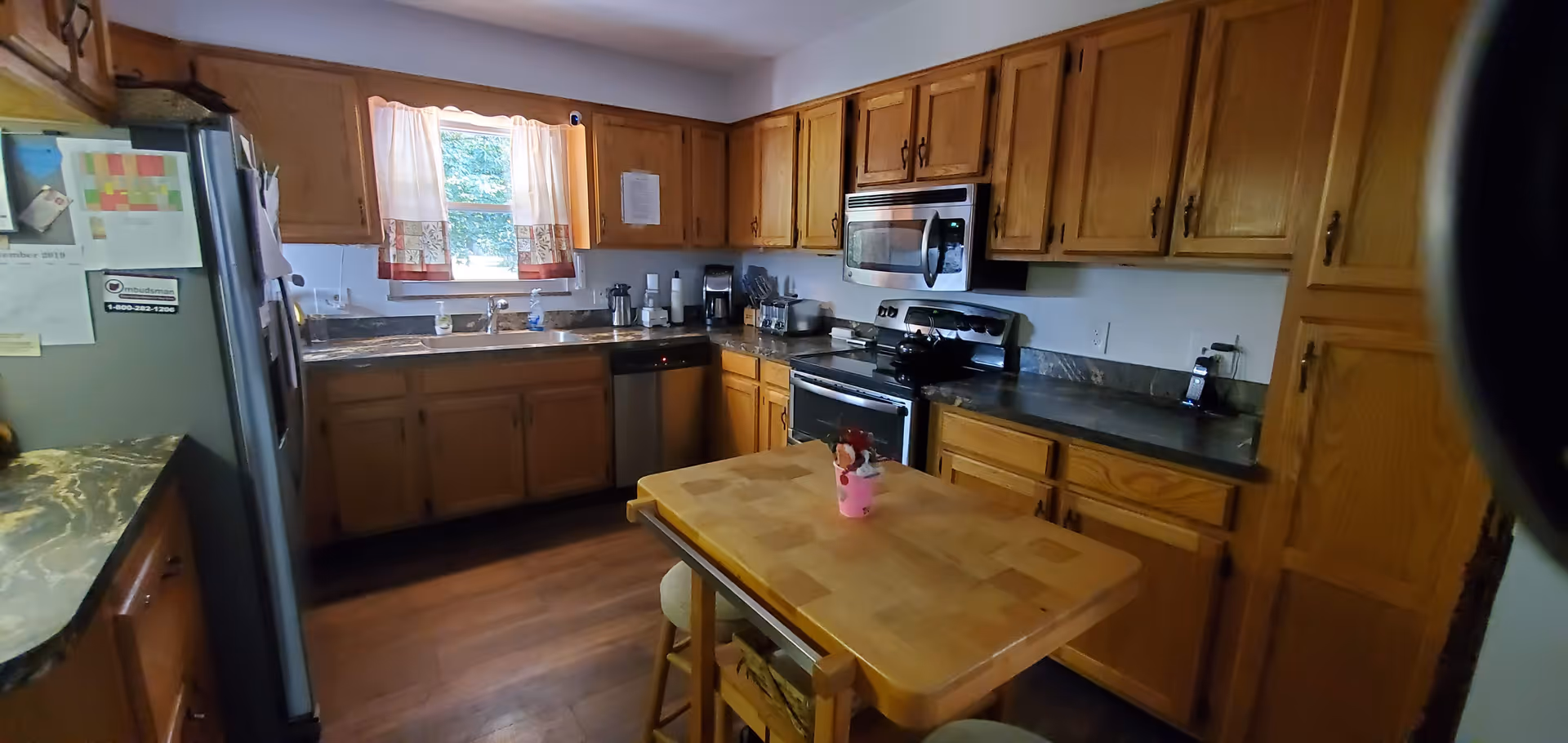 Kitchen with wooden cabinets, stainless steel appliances, a central wooden island and a window above the sink.