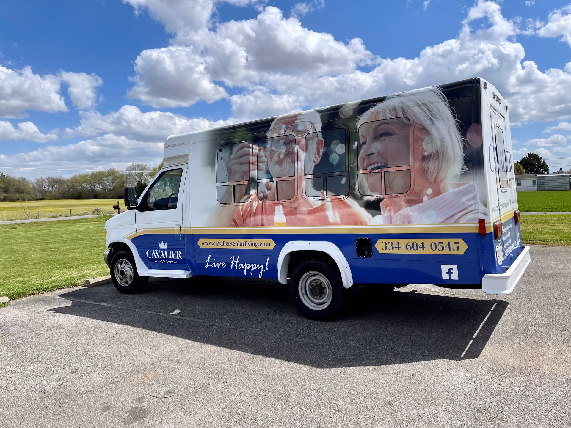 A Cavalier Senior Living shuttle van with large photos of smiling older adults on its side parked on a paved lot under a partly cloudy sky.