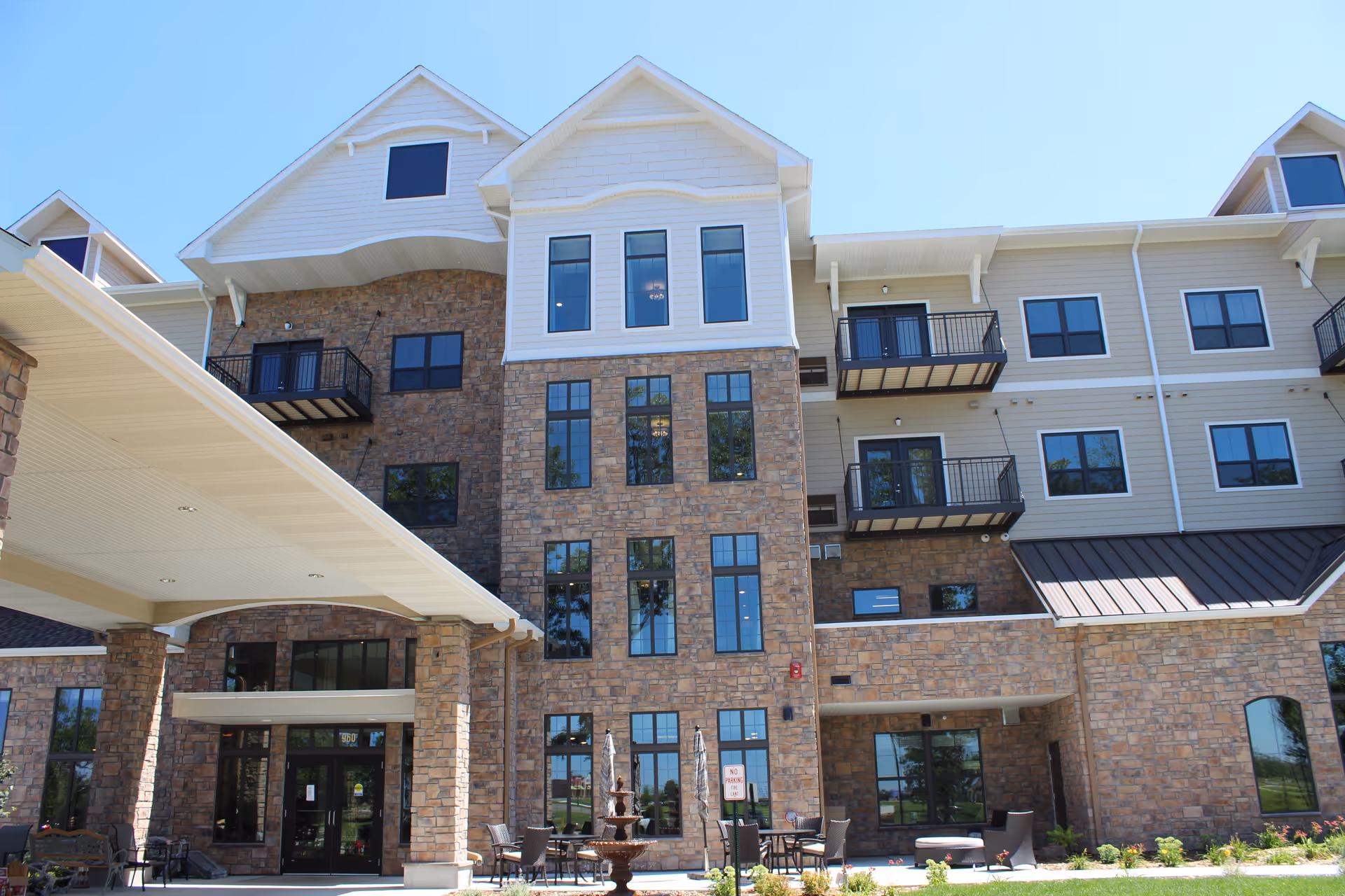 Three-story stone-and-siding senior living building front with an entrance canopy, balconies, and outdoor seating.