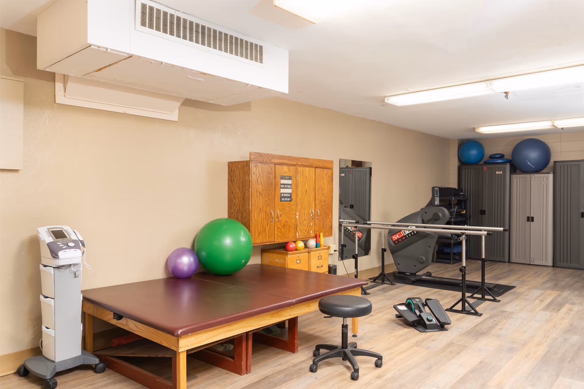 Small physical therapy room with a treatment table, exercise balls, therapy equipment, and storage cabinets.