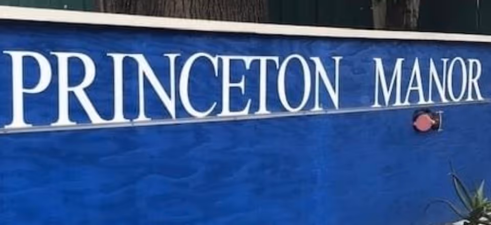 A close-up view of a blue sign with white letters that reads 'PRINCETON MANOR'.