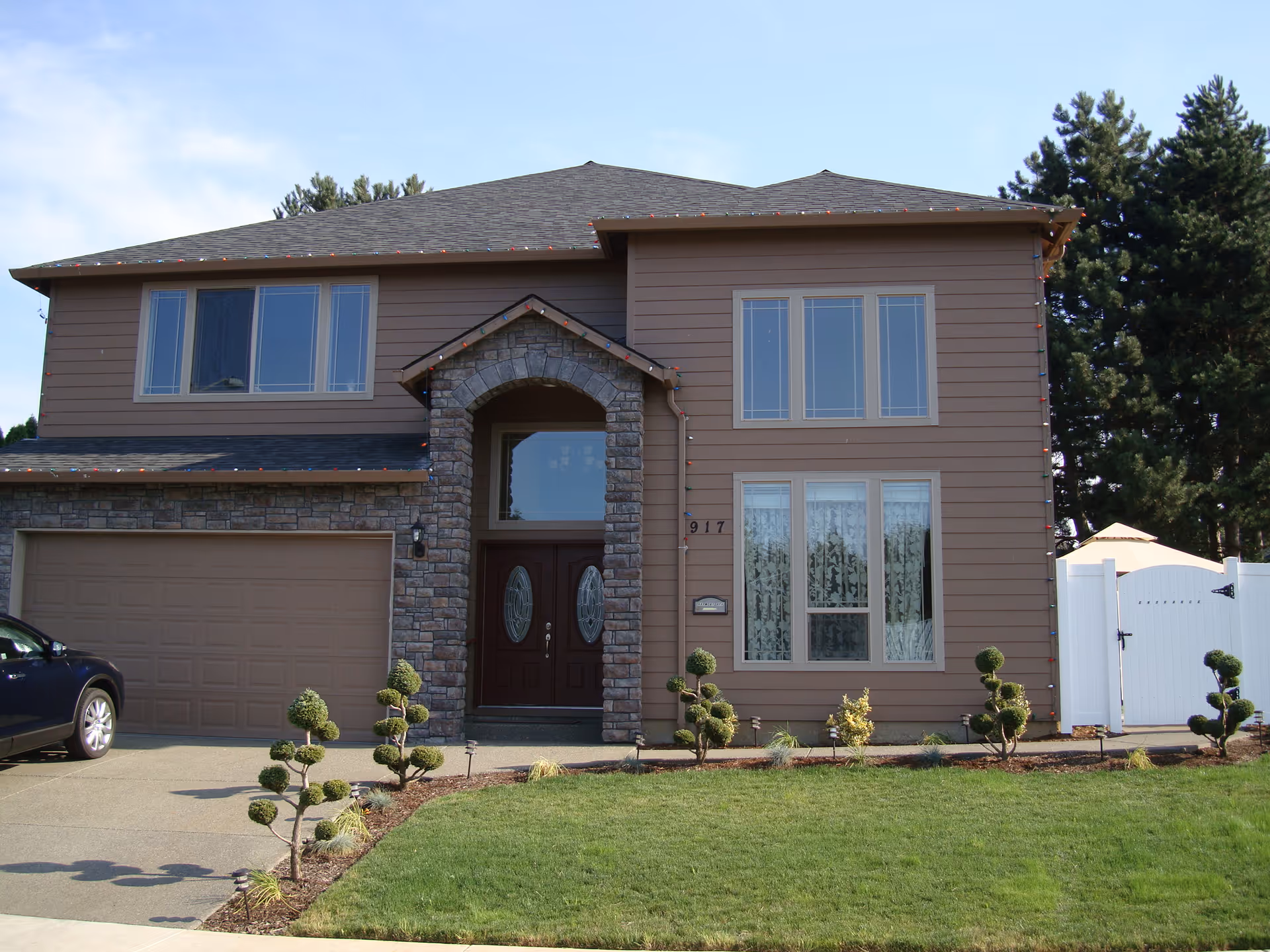 Front exterior of a two-story suburban house with a stone arched entry, double garage, and trimmed lawn.