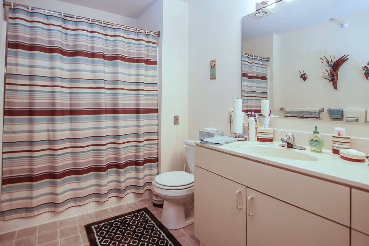 A clean bathroom with a striped shower curtain, toilet, sink vanity, and mirror.
