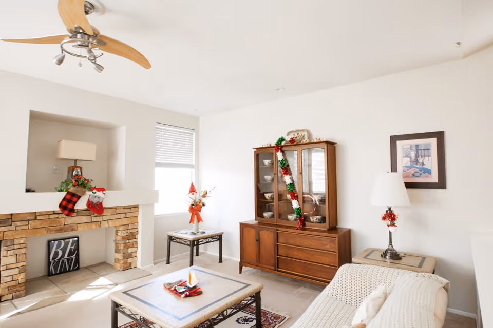 Bright living room with a stone fireplace, coffee table, sofa, wooden china cabinet, and holiday decorations.