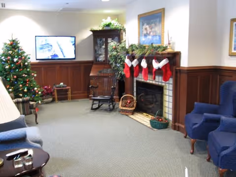 Cozy senior living room/lounge decorated for Christmas with a fireplace, stockings, a tree, and seating.