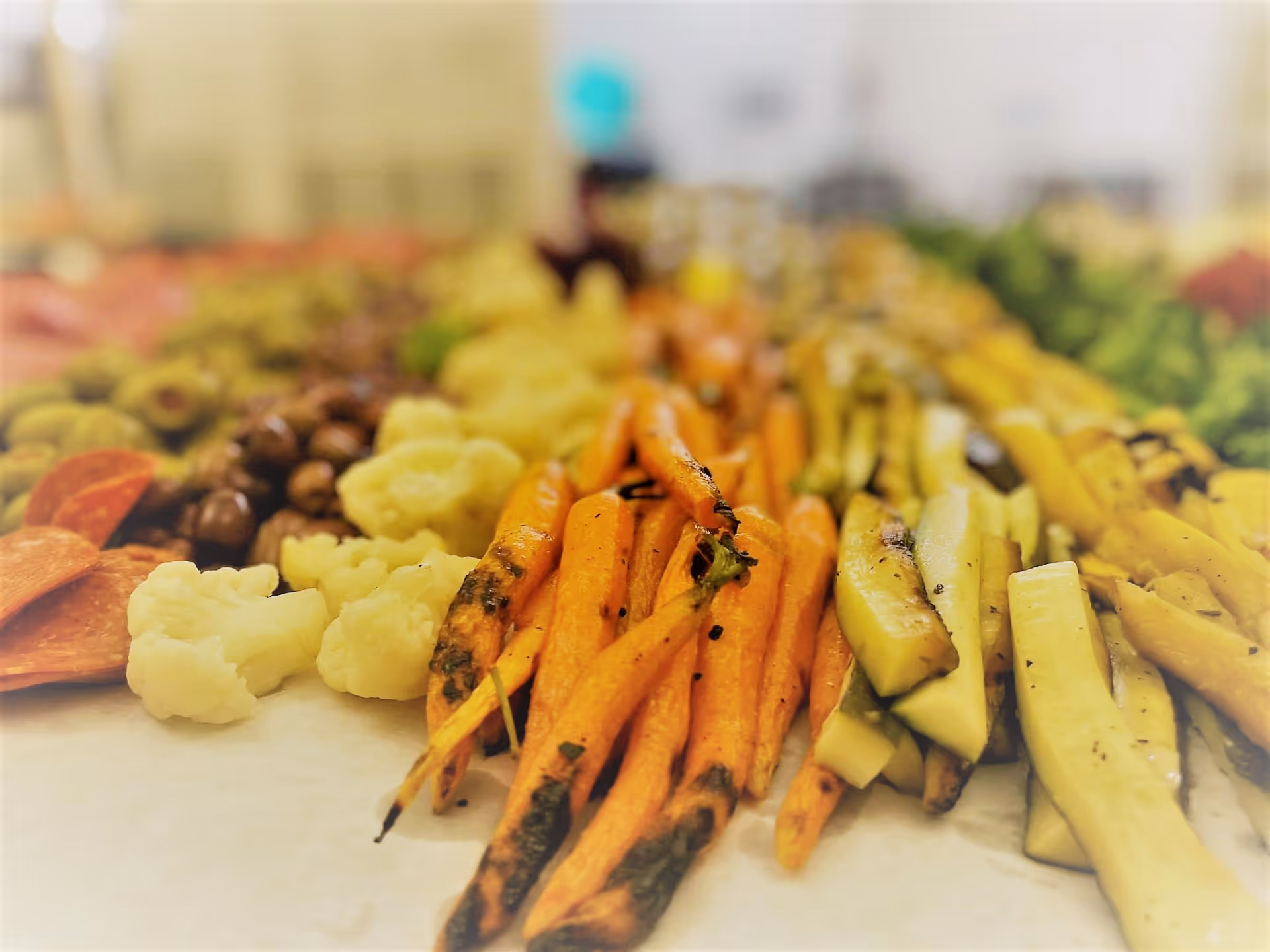 Close-up of a buffet platter with roasted carrots, zucchini, cauliflower and assorted vegetables and cold cuts.