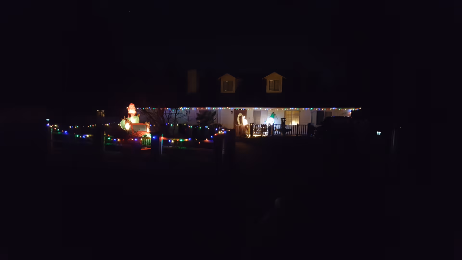 Front of a house at night decorated with multicolored Christmas lights and an inflatable Santa on the lawn.
